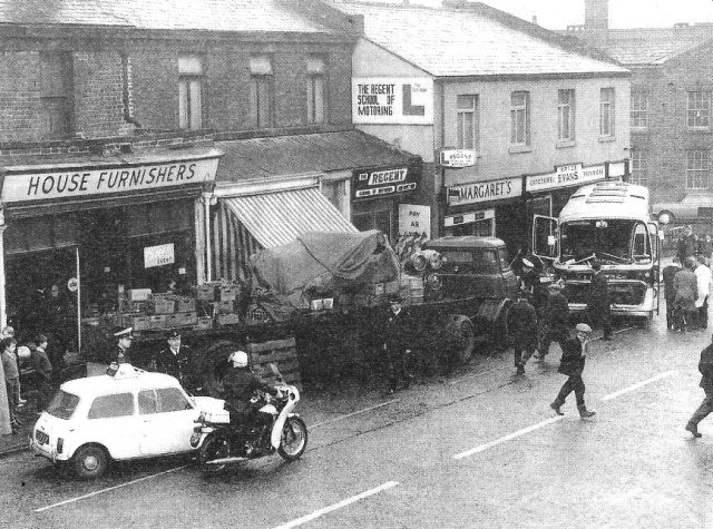 Morris Mini Cooper S MkII with twin fuel tanks and roof-mounted police equipment in a busy street scene beside a police motorcycle.